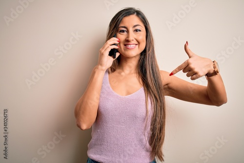 Young brunette woman having conversation talking on the smartphone over white background with surprise face pointing finger to himself © Krakenimages.com