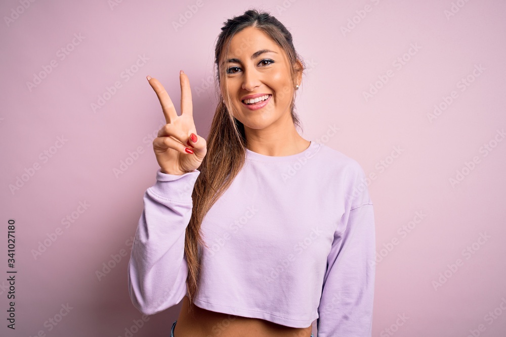 Young beautiful sport woman wearing sweatshirt over pink isolated background showing and pointing up with fingers number two while smiling confident and happy. Young beautiful sport woman wearing sweatshirt over pink isolated background showing and pointing up with fingers number two while smiling confident and happy.