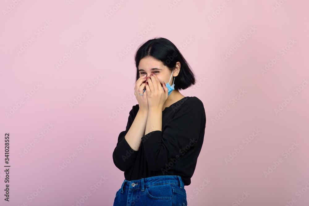 The caucasian girl in blue colored protective face mask. The girl looking at camera. Portrait shot over pink background. virus and pollution protection concept. The caucasian girl in blue colored protective face mask. The girl looking at camera. Portrait shot over pink background. virus and pollution protection concept.