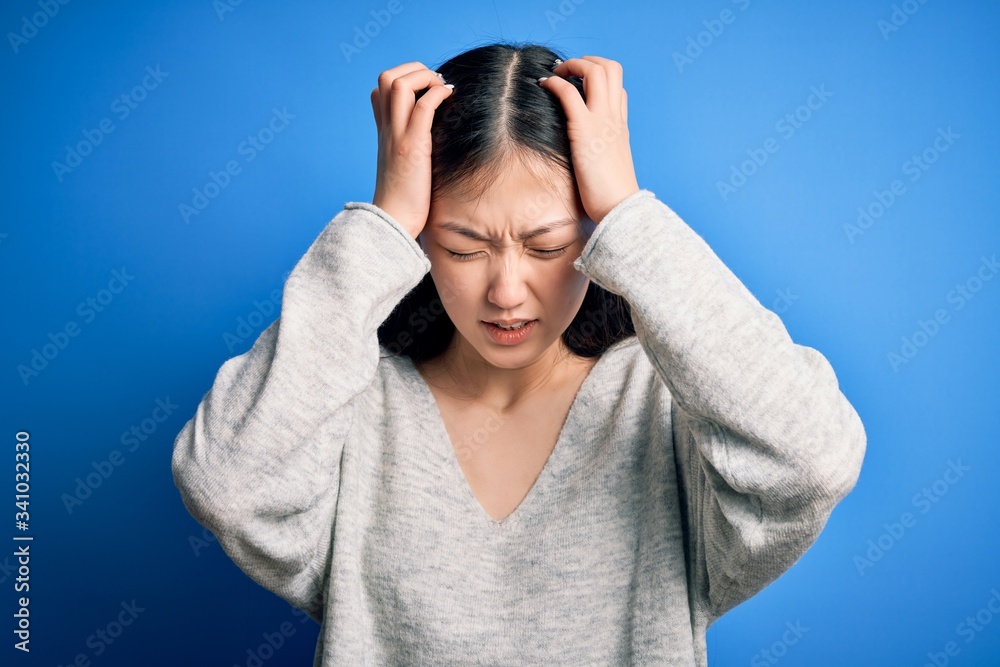 Φωτογραφία Young beautiful asian woman wearing casual sweater standing over blue isolated background suffering from headache desperate and stressed because pain and migraine
