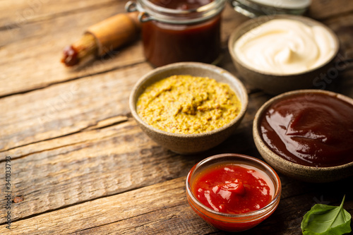 Classic set of sauces, American yellow mustard, ketchup, barbecue sauce, mayonnaise on wooden background, top view with copy space.
