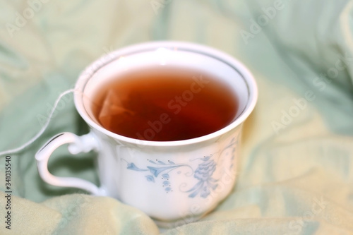 Tea in a vintage porcelain cup on a bed. Selective focus.
