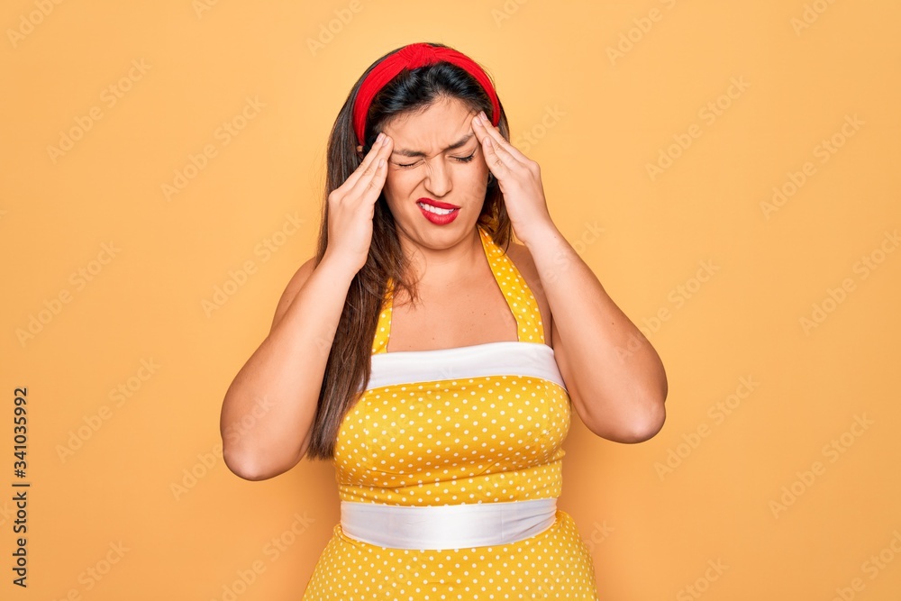 Young hispanic pin up woman wearing fashion sexy 50s style over yellow background with hand on headache because stress. Suffering migraine. Young hispanic pin up woman wearing fashion sexy 50s style over yellow background with hand on headache because stress. Suffering migraine.