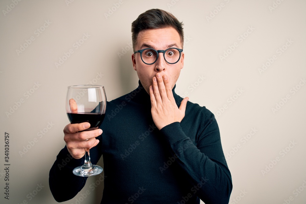 Young handsome caucasian man drinking an alcoholic glass of red wine over isolated background cover mouth with hand shocked with shame for mistake, expression of fear, scared in silence, secret Young handsome caucasian man drinking an alcoholic glass of red wine over isolated background cover mouth with hand shocked with shame for mistake, expression of fear, scared in silence, secret