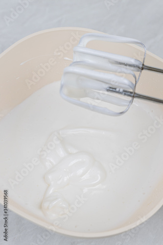 White whipped cream in the bowl with mixer above