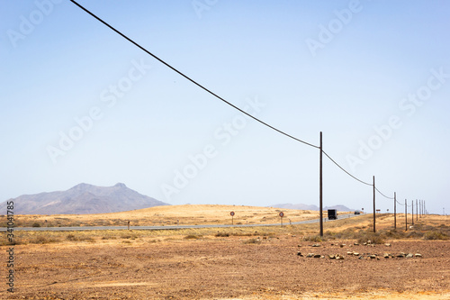 Truck following car on desert road with electric wooden posts along in Fuerteventura island. Arid landscape with volcanic mountain on background in Canary Islands, Spain