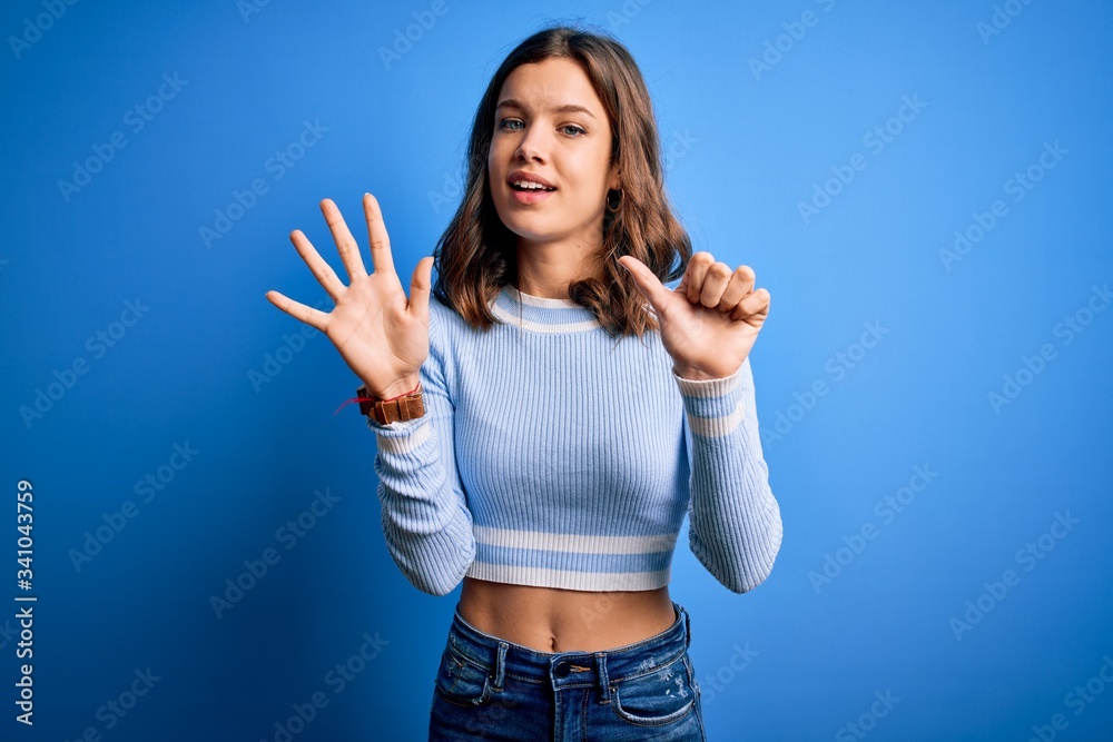 Young beautiful blonde girl wearing casual sweater standing over blue isolated background showing and pointing up with fingers number six while smiling confident and happy. Young beautiful blonde girl wearing casual sweater standing over blue isolated background showing and pointing up with fingers number six while smiling confident and happy.