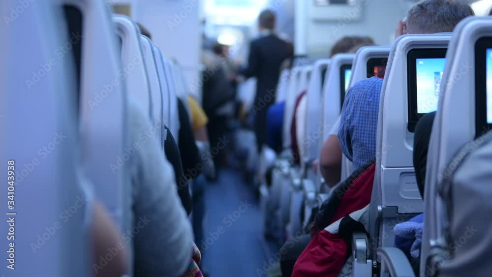 Isle or a corridor of a loading passenger airplane ready for takeoff. Flight attendant helping people to put away luggage and find seats. Interior of a airliner or commercial plane with people seated