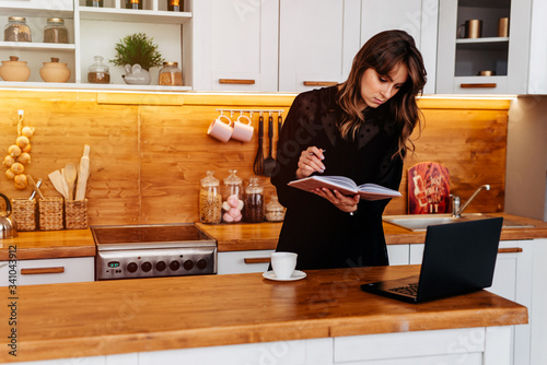 Beautidul adultwoman is working on laptop in kitchen, dur the businessplan photo