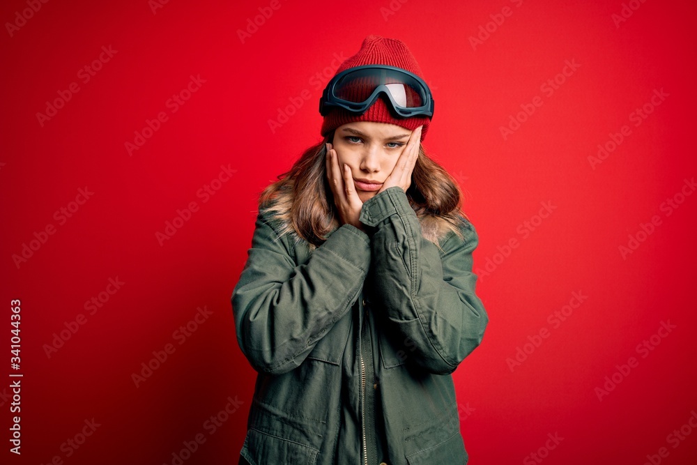 Young blonde girl wearing ski glasses and winter coat for ski weather over red background Tired hands covering face, depression and sadness, upset and irritated for problem Young blonde girl wearing ski glasses and winter coat for ski weather over red background Tired hands covering face, depression and sadness, upset and irritated for problem
