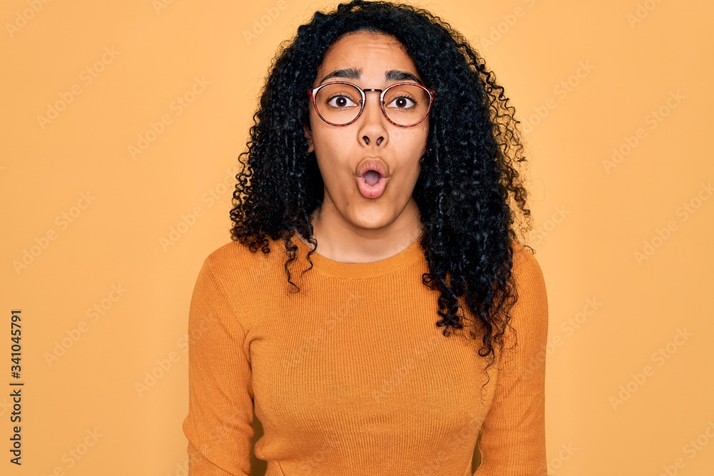 Young african american woman wearing casual sweater and glasses over yellow background afraid and shocked with surprise expression, fear and excited face. Young african american woman wearing casual sweater and glasses over yellow background afraid and shocked with surprise expression, fear and excited face.