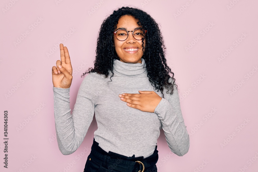Young african american woman wearing turtleneck sweater and glasses over pink background smiling swearing with hand on chest and fingers up, making a loyalty promise oath