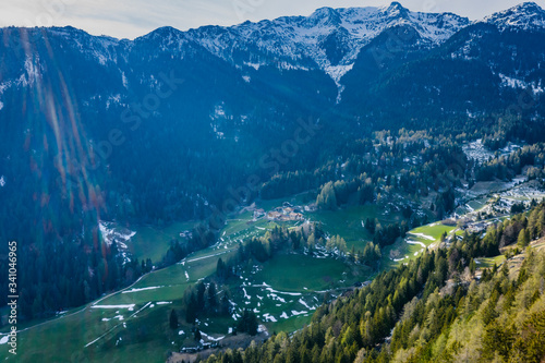 Aerial view of huge valley of the mountains of Italy, Trentino, green meadows, Slopes with green spruce trees, Dolomites on background, The town in the bottom of a valley photo