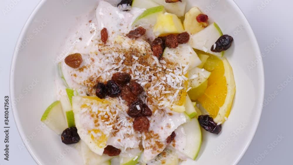 Mixed and assorted fruits in bowl rotating. Top view. Healthy salad dessert. Kiwi, orange, pear and banana slices with yoghurt and raisins. Healthy nutrition