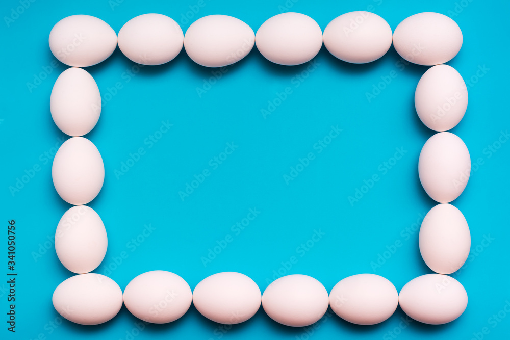 The original volumetric frame of white chicken eggs on a blue background. Top view. Copy space The original volumetric frame of white chicken eggs on a blue background. Top view. Copy space