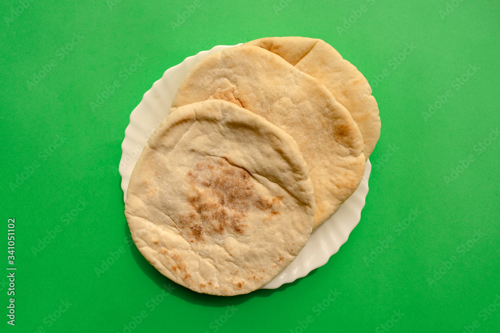 Famous traditional Arabic pita bread in white plate on green background
