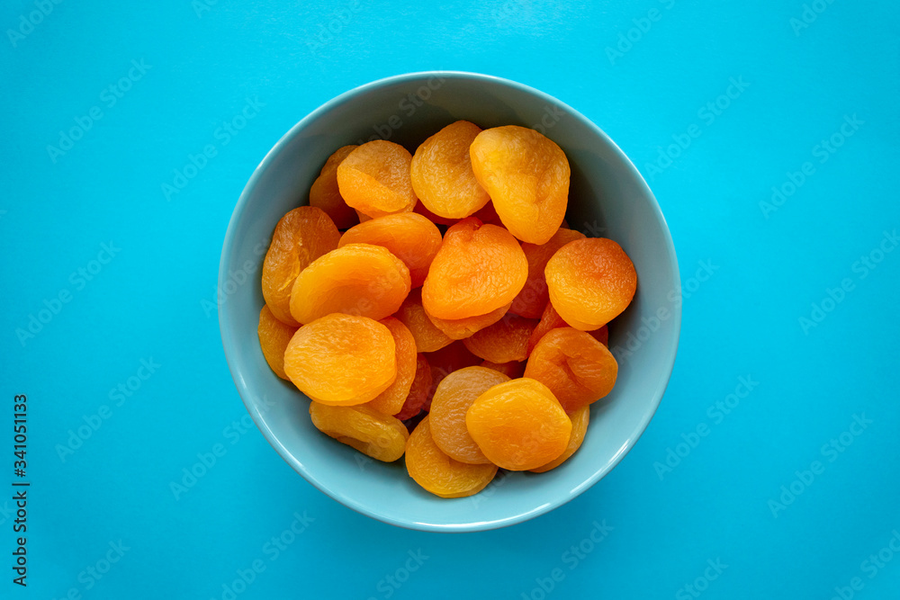 Dry apricots in turquoise bowl on blue background, top view. Heap of dried apricots. Dry apricots in turquoise bowl on blue background, top view. Heap of dried apricots.