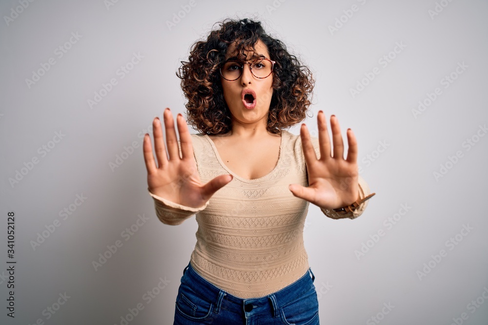 Young beautiful curly arab woman wearing casual t-shirt and glasses over white background doing stop gesture with hands palms, angry and frustration expression Young beautiful curly arab woman wearing casual t-shirt and glasses over white background doing stop gesture with hands palms, angry and frustration expression