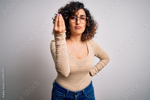 Young beautiful curly arab woman wearing casual t-shirt and glasses over white background Doing Italian gesture with hand and fingers confident expression
