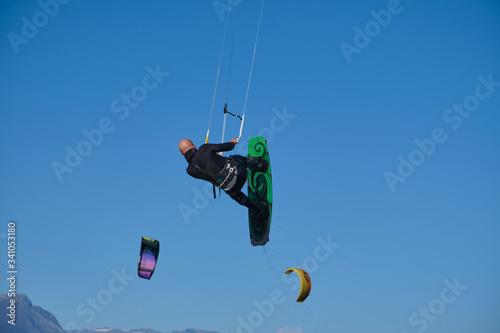 Kitesurfer in wetsuit in the jump on a background of high mountains in company with Kitesurfers