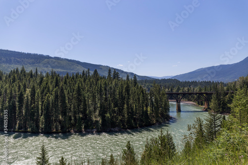 river that runs through a pine forest, in the distance a bridge crosses it