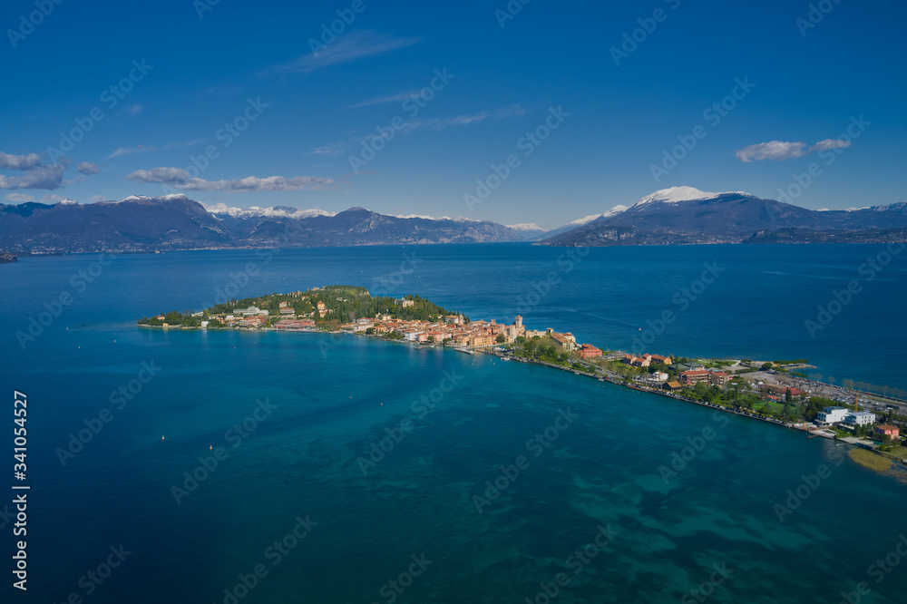 Sirmione town, Lake Garda, Italy. Aerial view of Sirmione Castle. The historical part of the city.  In the background mountains in the snow and blue sky. Side view of the island. Aerial panorama