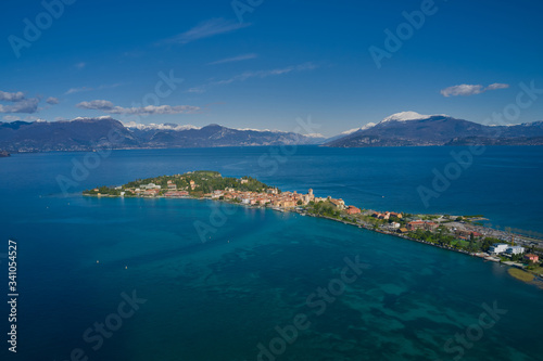 Sirmione town, Lake Garda, Italy. Aerial view of Sirmione Castle. The historical part of the city. In the background mountains in the snow and blue sky. Side view of the island. Aerial panorama