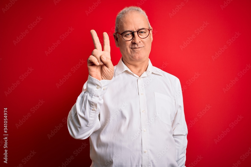 Fototapeta premium Middle age handsome hoary man wearing casual shirt and glasses over red background smiling looking to the camera showing fingers doing victory sign. Number two.