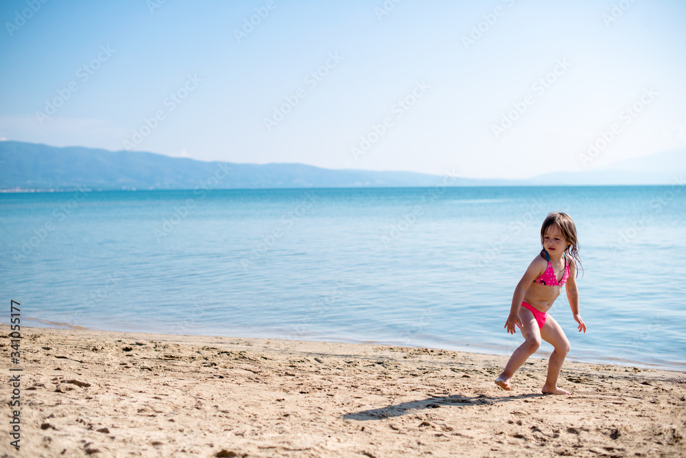 Happy little girl with pink swim suite playing on a beach
