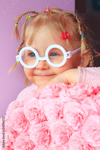 Little girl in plastic glasses smile near paper flowers made from papier-mache.