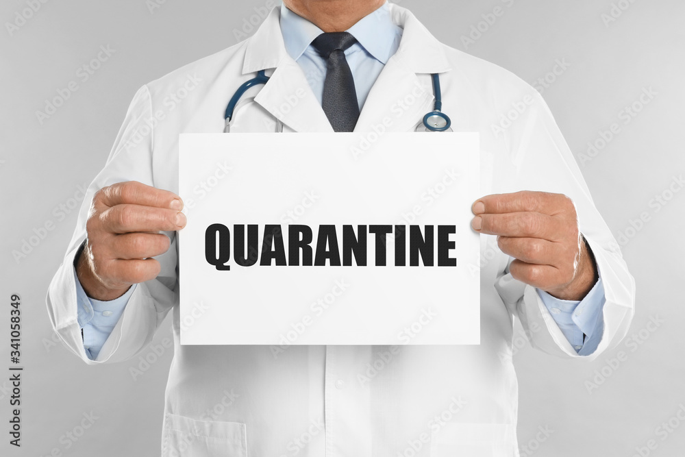 Doctor holding sign with text QUARANTINE on light grey background, closeup. Stay at home during coronavirus outbreak Doctor holding sign with text QUARANTINE on light grey background, closeup. Stay at home during coronavirus outbreak
