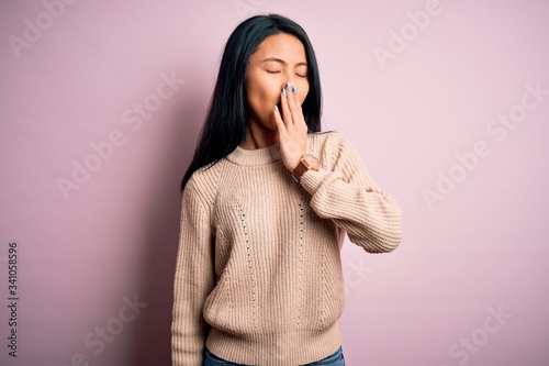 Young beautiful chinese woman wearing casual sweater over isolated pink background bored yawning tired covering mouth with hand. Restless and sleepiness.