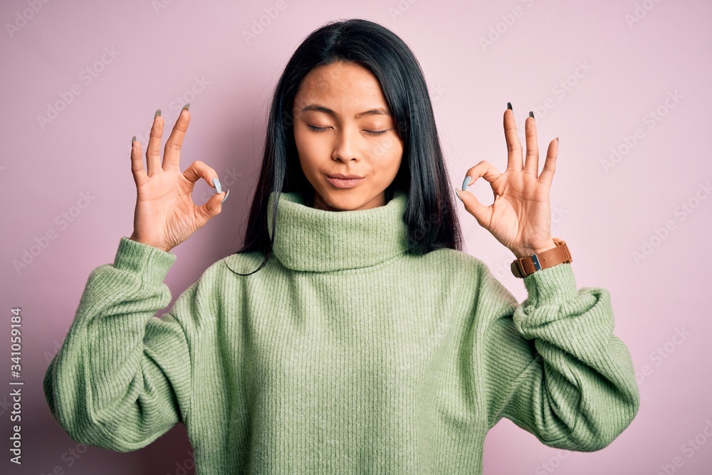 Young beautiful chinese woman wearing turtleneck sweater over isolated pink background relax and smiling with eyes closed doing meditation gesture with fingers. Yoga concept. Young beautiful chinese woman wearing turtleneck sweater over isolated pink background relax and smiling with eyes closed doing meditation gesture with fingers. Yoga concept.