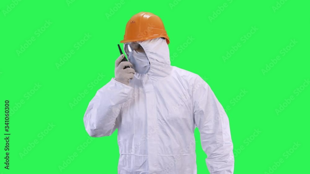 A man in a helmet and a protective suit in his hands holds a walkie-talkie goes forward.Green screen background. A man in a helmet and a protective suit in his hands holds a walkie-talkie goes forward.Green screen background.