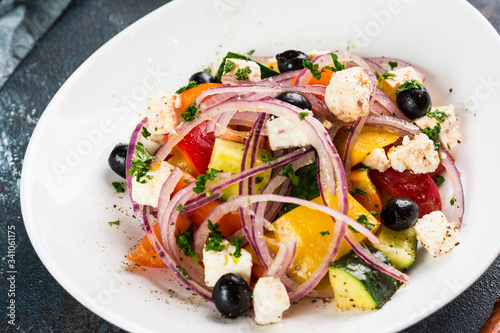 Greek salad with juicy tomatoes, feta cheese, lettuce, green olives, cucumber, red onion and fresh parsley. Homemade food. Symbolic image. Concept for a tasty and healthy vegetarian meal. Close up.