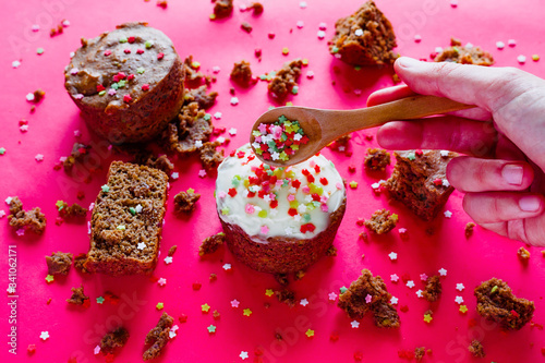 Candy composition with pastel color background. Healthy spelled flour muffins topped with mascarpone cheese and colored stars. Hand of a young woman picking up a bamboo wooden spoon. Copy space