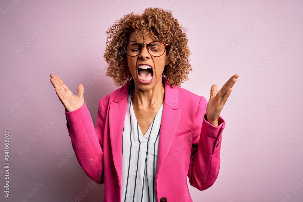 Young african american businesswoman wearing glasses standing over pink background celebrating mad and crazy for success with arms raised and closed eyes screaming excited. Winner concept Young african american businesswoman wearing glasses standing over pink background celebrating mad and crazy for success with arms raised and closed eyes screaming excited. Winner concept