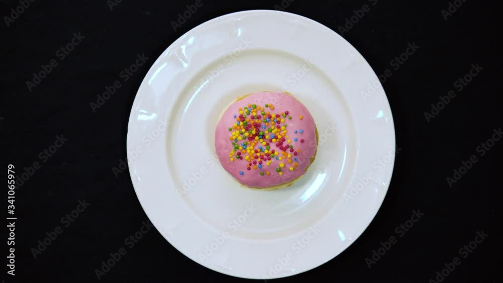 white plate on black background. Male hand put delicious sweet donut on a plate. Top view. Bright and colorful sprinkled donut close-up macro shot spinning on a black background 4k white plate on black background. Male hand put delicious sweet donut on a plate. Top view. Bright and colorful sprinkled donut close-up macro shot spinning on a black background 4k