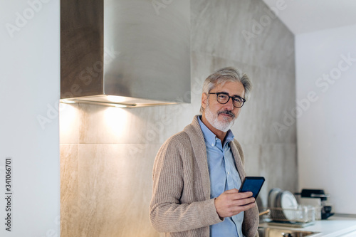 Portrait of mature man with cell phone in kitchen at home
