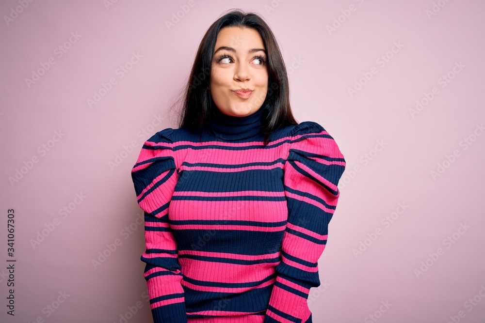 Young brunette elegant woman wearing striped shirt over pink isolated background smiling looking to the side and staring away thinking. Young brunette elegant woman wearing striped shirt over pink isolated background smiling looking to the side and staring away thinking.
