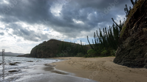 Tortoise bay - Famous new caledonian beach with typical colonary pine. dark green hill in the background. beautiful stormy clouds in the sky