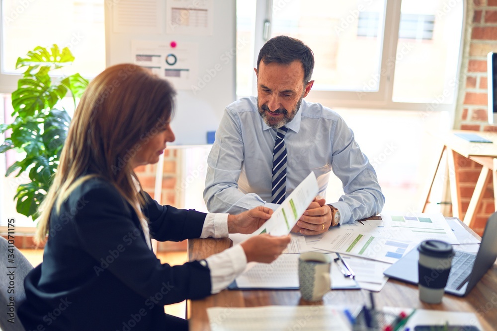 Two middle age business workers smiling happy and confident. Working together with smile on face using laptop at the office Two middle age business workers smiling happy and confident. Working together with smile on face using laptop at the office