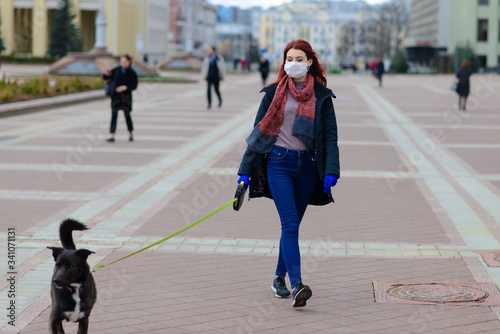 Young female using a face mask as a coronavirus spreading prevention walking with her dog. Global COVID-19 pandemic concept image.