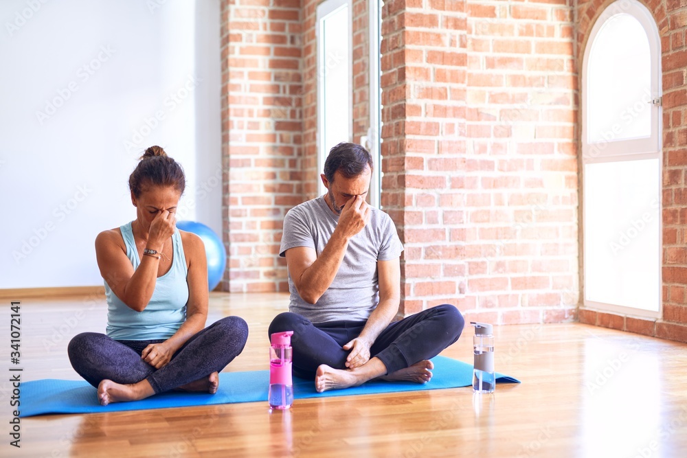 Middle age sporty couple sitting on mat doing stretching yoga exercise at gym tired rubbing nose and eyes feeling fatigue and headache. Stress and frustration concept. Middle age sporty couple sitting on mat doing stretching yoga exercise at gym tired rubbing nose and eyes feeling fatigue and headache. Stress and frustration concept.