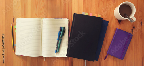 tidy workspace to study or work at home from a top view - open blank striped notebook with pens and books on a wooden background table for planning, food for a banner, wallpaper or head of a blog