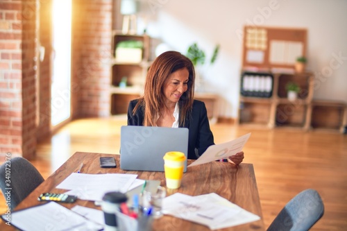 Middle age beautiful businesswoman smiling happy and confident. Sitting on chair working in a desk at the office