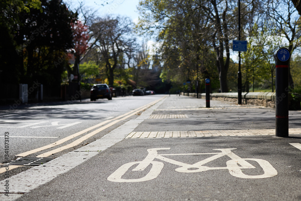 Obraz premium Cycle lane sign painted on bike lane. Urban street with trees and double yellow lines and parked cars.
