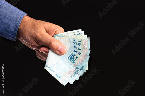 hand holding several hundred reais bills from Brazil, on isolated black background. Emergency government aid paid to microentrepreneurs, worth 600 reais photo