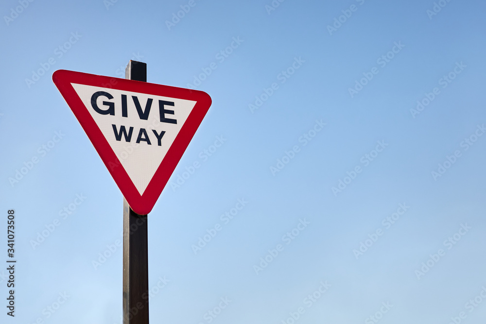 Isolated British give way traffic sign against blue sky background. Space for copy text. Red upside down triangle. Isolated British give way traffic sign against blue sky background. Space for copy text. Red upside down triangle.