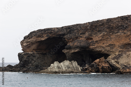 Ajuy black cave on cliff edge with sharp rock formation by the sea in Fuerteventura, Spain. Famous tourism attraction on volcanic island. Hiking, explore concepts